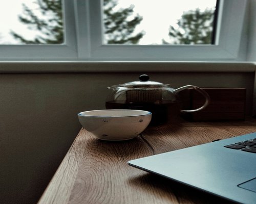 A closed laptop computer resting on a warm wooden table near a fresh cup of tea