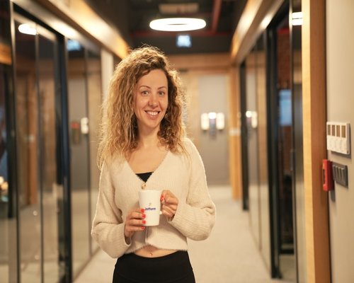 A smiling person holding a ceramic mug looking relaxed during a work intermission