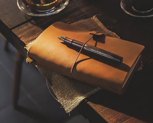 A flatlay shot showing a neat diary notebook and an aluminum fountain pen on an office surface